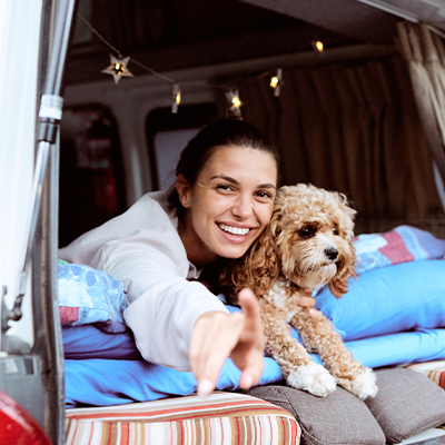 Woman and her dog cuddle in the back of their Hippie Hitop Campervan at a campground
